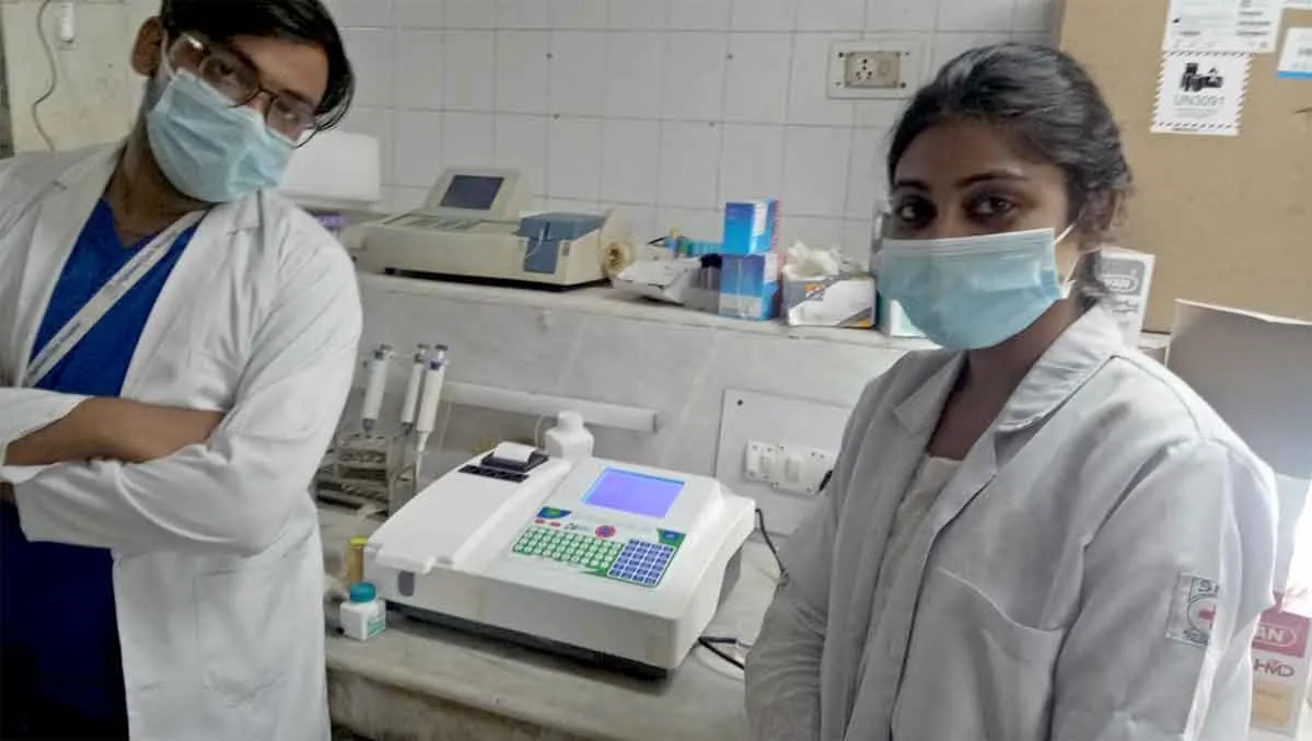 Two laboratory staff in lab coats beside a semi-automatic analyser